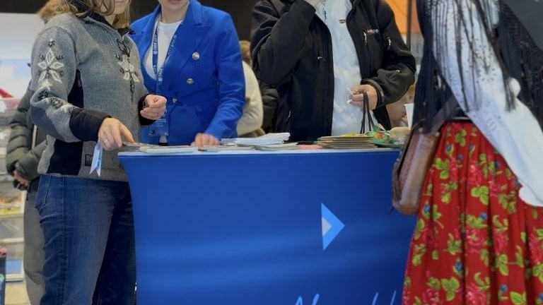 Grupa ludzi rozmawiająca przy stoisku promocyjnym.jpg