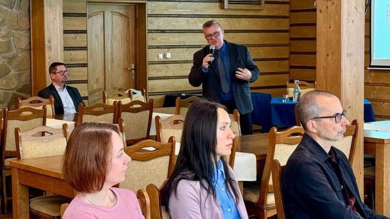 Grupa ludzi siedząca przy stole oraz jedna z mikrofonem, która przemawia.jpg